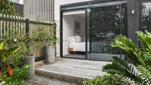 Une chambre à coucher moderne aménagée à l’extérieur, dotée d’une porte-fenêtre coulissante, d’une terrasse en bois et entourée de verdure.