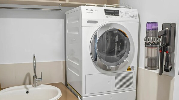 Une buanderie moderne équipée d’un lave-linge Miele, d’un évier et d’un distributeur d’eau.