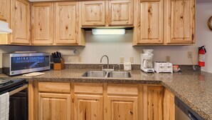 A kitchen with wooden cabinets, a microwave, a sink, a coffee maker, and a toaster. - Ski, Soak & Chill! Pool-View Winter Park Condo (Winter Park)