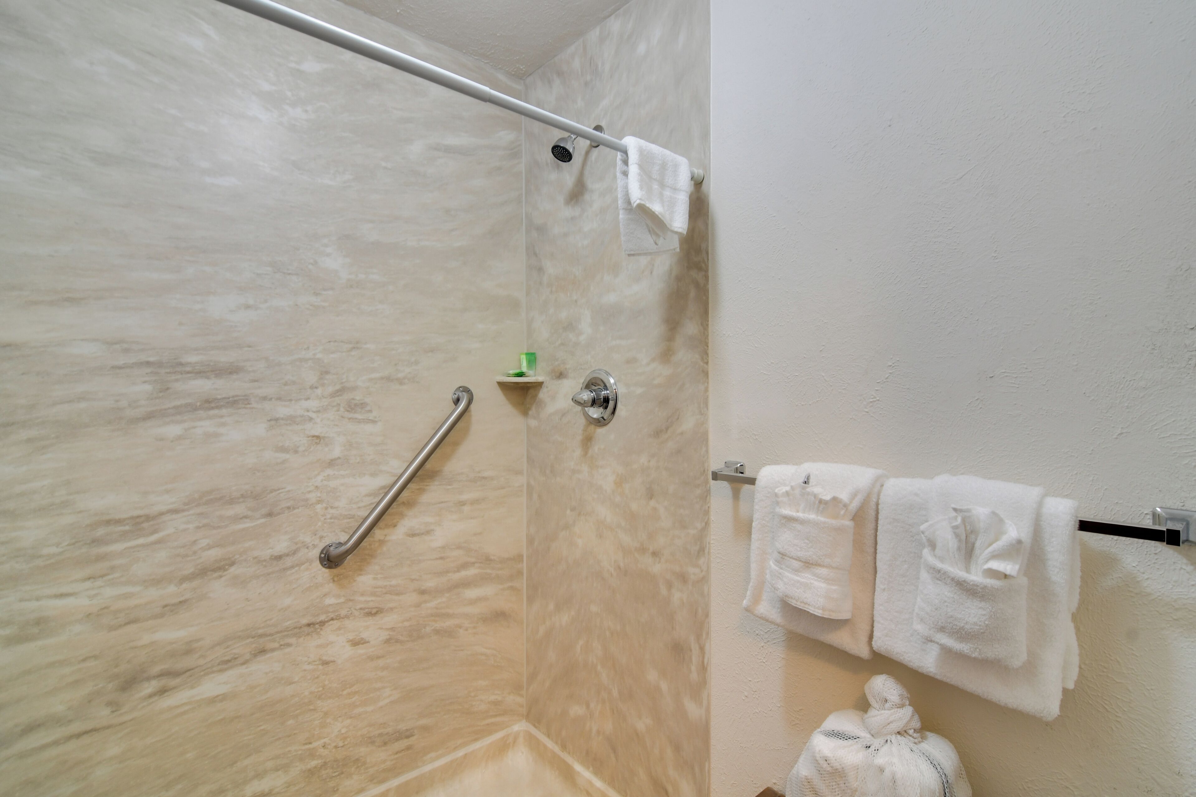 A bathroom with a shower, a handrail, and a towel rack with towels.