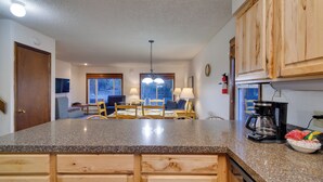 A kitchen with granite countertops, wooden cabinets, a coffee maker, and a dining area with a table and chairs. - Woodsy Winter Park Condo w/ Pool & Hot Tub Access (Winter Park)