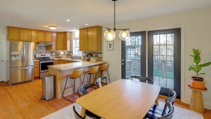 A modern kitchen with wooden cabinets, stainless steel appliances, a central island with bar stools, and a large dining table. - Covered Deck & Fire Pit: Weaverville Getaway! (Weaverville)