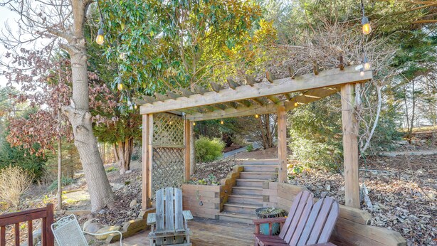 A wooden deck with outdoor seating, a pergola with string lights, and a staircase leading to a higher level. - Covered Deck & Fire Pit: Weaverville Getaway! (Weaverville)