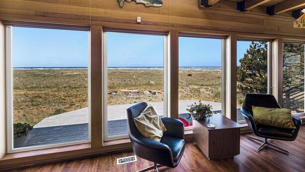 A room with large windows offering a view of the ocean and a wooden ceiling with a fish decoration. There are two chairs and a small table with a plant. - Fantastic Beach View! Oregon Escape w/ Game Room (Seaside)