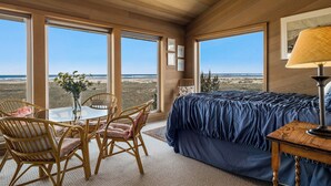 A bedroom with a large bed, a table with chairs, and a view of the desert landscape through large windows. - Fantastic Beach View! Oregon Escape w/ Game Room (Seaside)