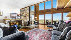 A spacious living room with a stone fireplace, large windows, and a cozy seating area. - Fantastic Beach View! Oregon Escape w/ Game Room (Seaside)