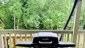 A Char-Broil grill on a wooden deck with a white railing, surrounded by greenery.