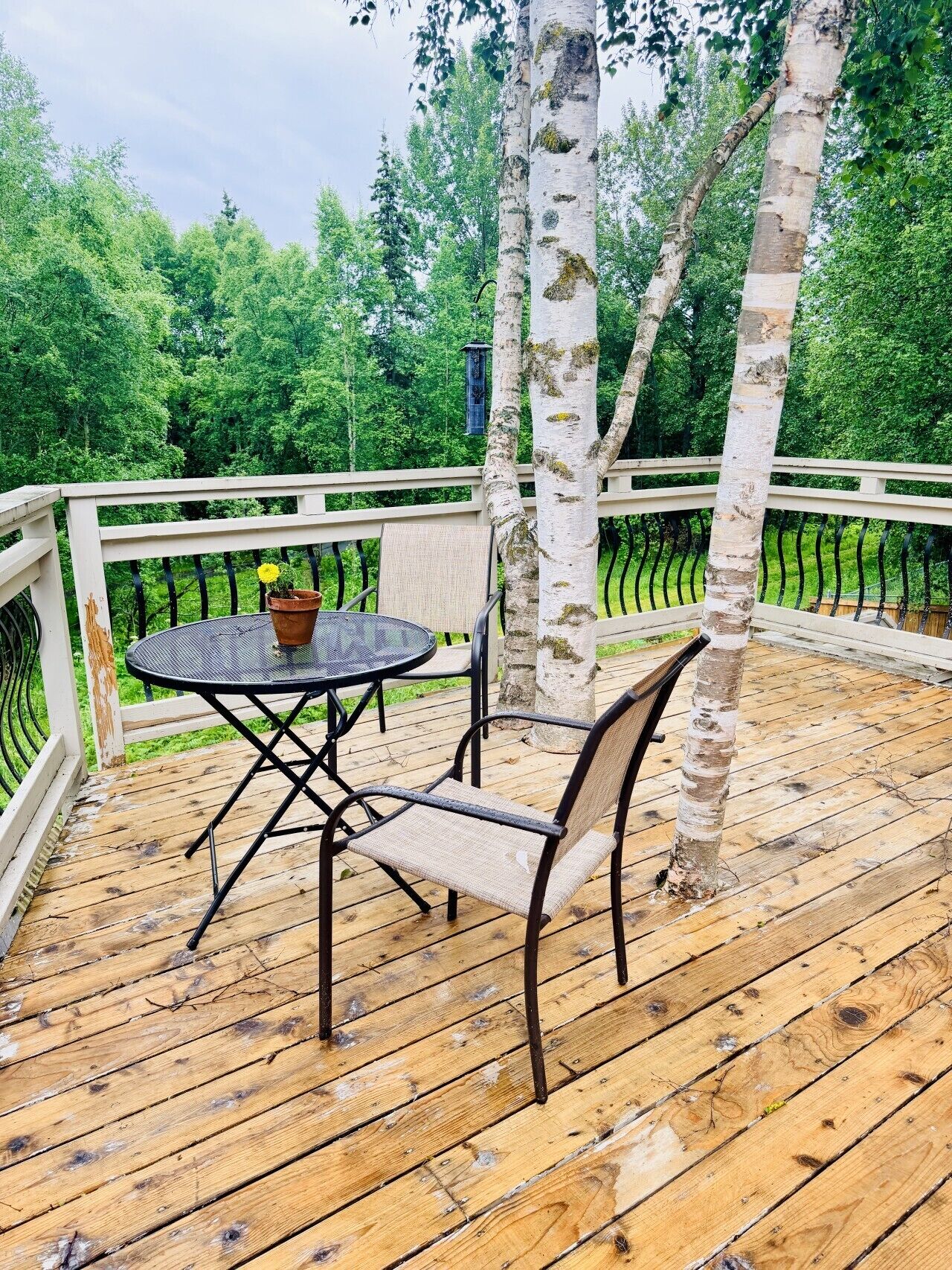 A wooden deck with a round table and two chairs, surrounded by a white railing.
