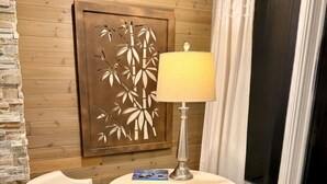 A room with a round table, two chairs, a lamp, a decorative wall panel, and a window with curtains.