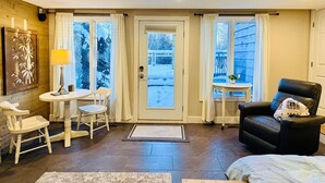 A cozy room with a dining area, a seating area with a chair, and a view through a door.