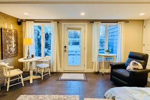 A cozy room with a dining area, a seating area with a chair, and a view through a door.