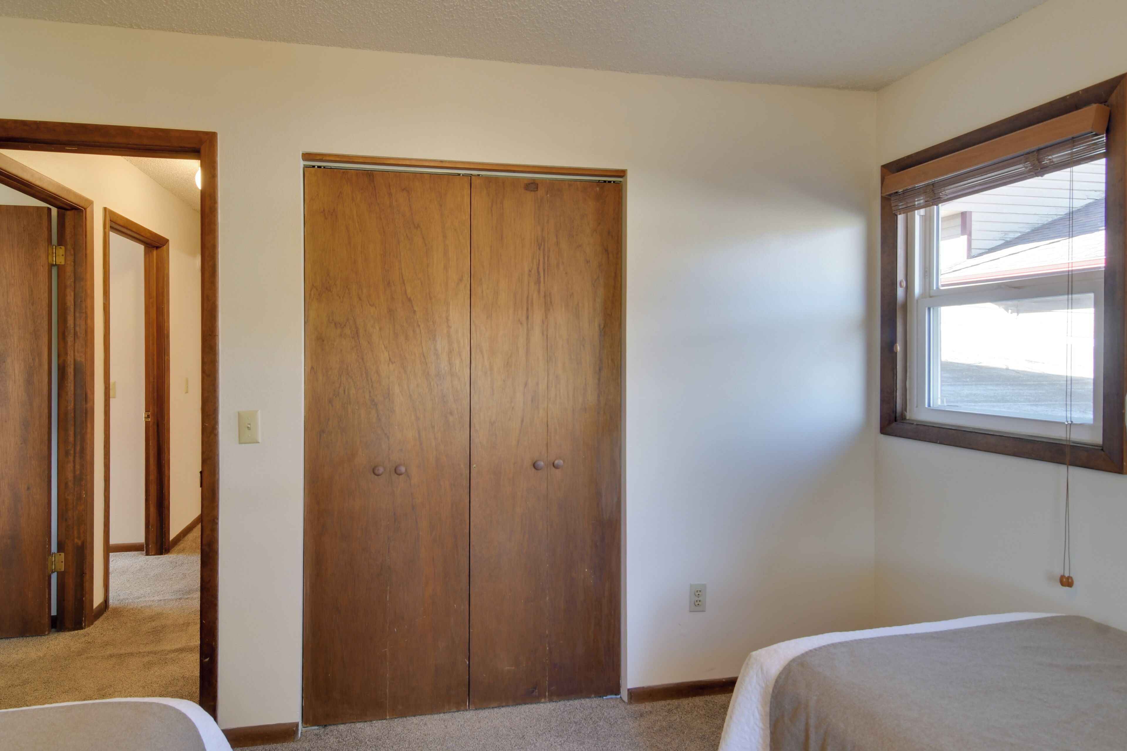 Un dormitorio con un armario de madera, una ventana y piso alfombrado.