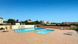 Una piscina al terrat amb dues piscines, envoltades per un solàrium amb rajoles i una tanca.