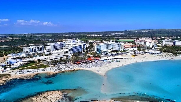 Vista aèria d'un hotel a la costa, amb diversos edificis, una platja i aigües blaves cristal·lines.
