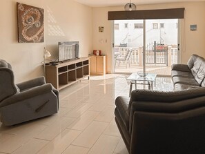 Una sala de estar con sofá, televisión, mesa de centro de vidrio y vista al exterior.