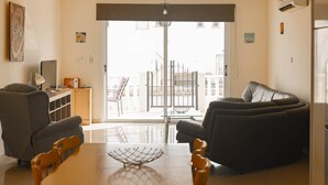 Uma sala de estar com uma mesa de jantar, dois sofás, uma televisão e uma varanda com portão.