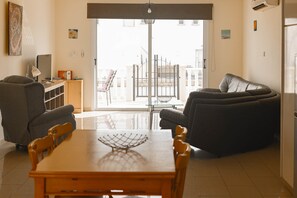 Una sala de estar con una mesa de comedor, dos sofás, un televisor y un balcón con reja.