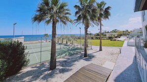 A tennis court with palm trees, a wooden deck, and a view of the sea. - Coralli Privileges Apt (Protaras)