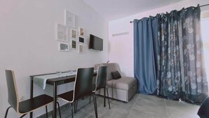 Une petite pièce moderne, équipée d’un bureau, de deux chaises, d’un canapé et d’un téléviseur fixé au mur.