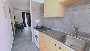 Une cuisine de taille réduite, équipée d’un évier, d’un lave-linge et de meubles de rangement en bois.