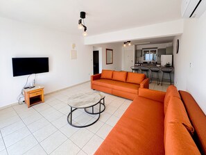 Un saló amb un sofà, una televisió, una taula de centre i una cuina al fons.