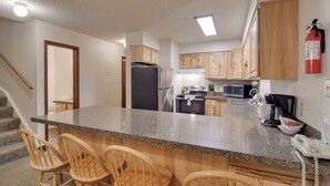 A kitchen with wooden cabinets, a granite countertop, a refrigerator, a microwave, a stove, and a coffee maker. - Shuttle to Winter Park Resort! Group Condo w/ Pool (Winter Park)