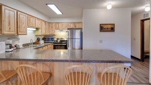 A modern kitchen with wooden cabinets, a granite countertop, stainless steel appliances, and a central island with bar stools. - 3 Mi to Skiing: Walkable Dtwn Winter Park Condo! (Winter Park)