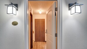 A hallway with a wooden door at the end, two wall-mounted lights, and a round brass plate on the wall. - 3 Mi to Skiing: Walkable Dtwn Winter Park Condo! (Winter Park)