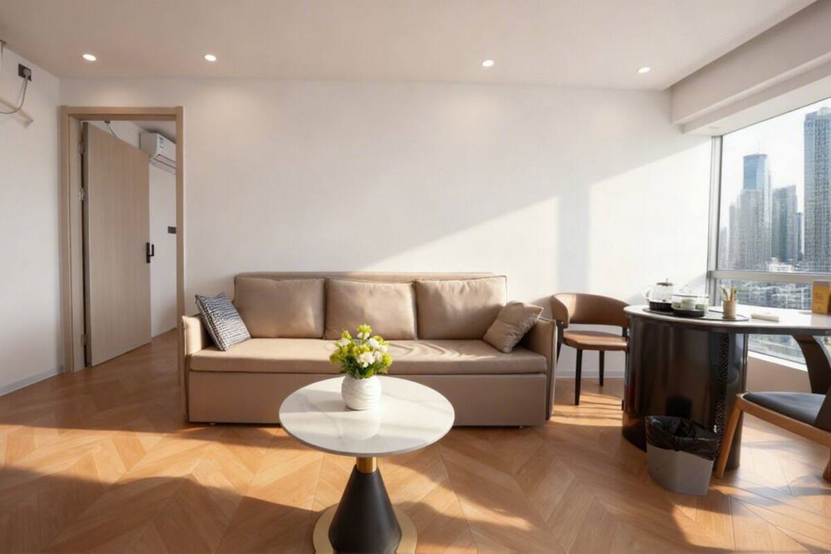 A modern living room with a sofa, a round coffee table, and a view of a cityscape through large windows.