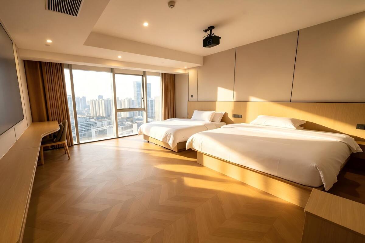 A hotel room with two beds, a TV, a desk, and a large window with a city view.