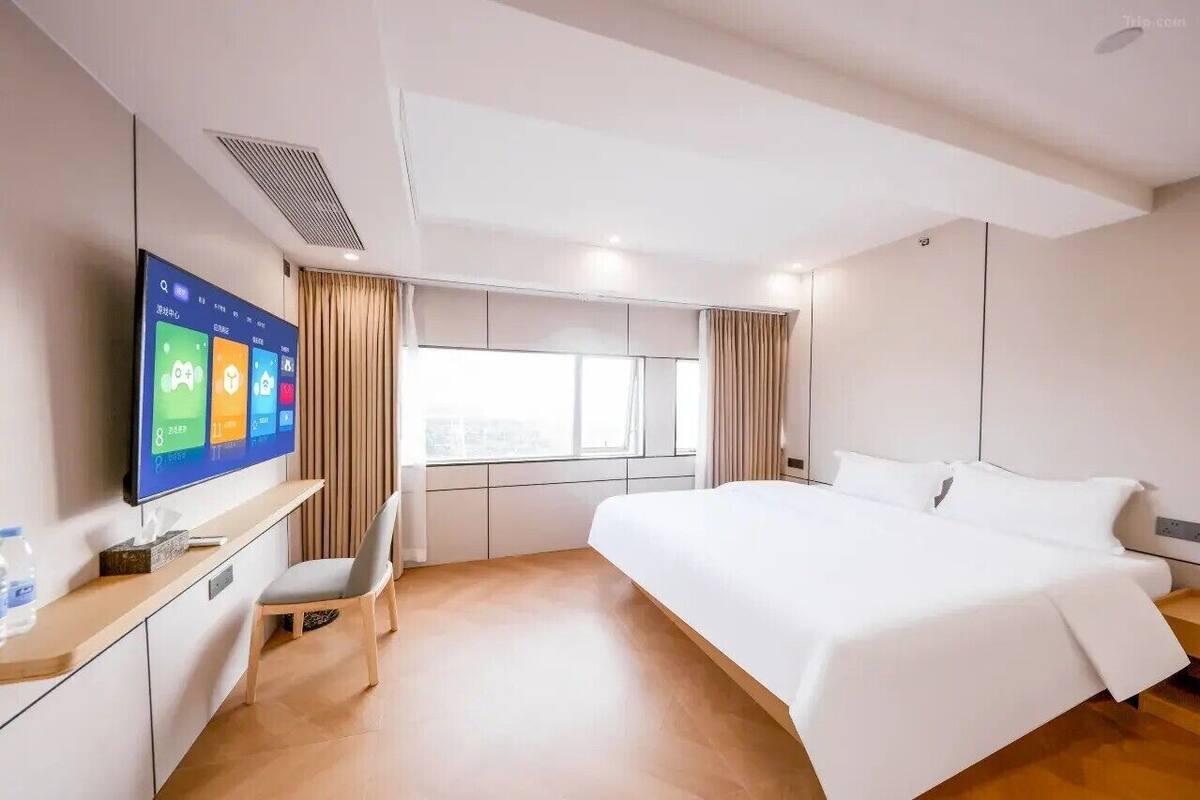 A hotel room with a bed, a TV mounted on the wall, a desk with a chair, and a window with curtains.