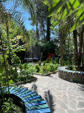 A paved pathway surrounded by lush greenery, a small play area, and a stone wall.