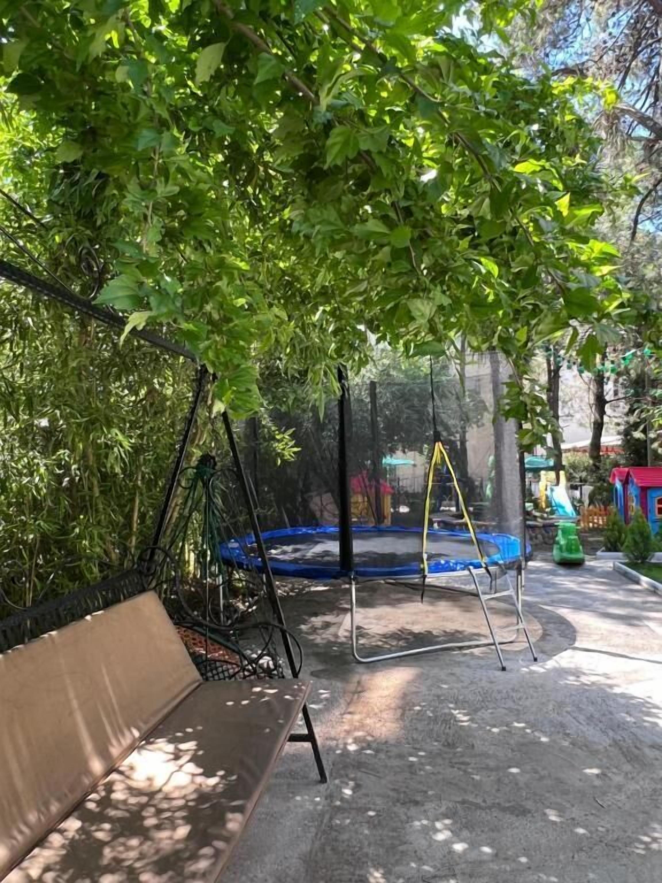 A park with a trampoline, a bench, and a swing set.