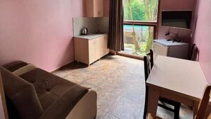 A room with a sofa, a dining table with chairs, a kitchenette, and a TV. - Inter (Ureki)