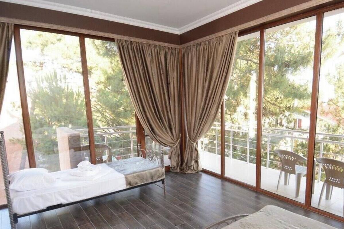 A room with a bed, large windows, and a balcony with chairs.