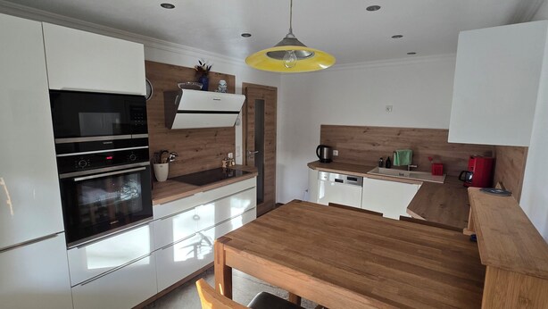 Een moderne keuken met witte kastjes, een houten eettafel en een gele hanglamp.
