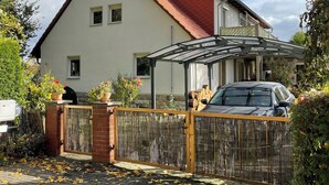 Een herenhuis met twee verdiepingen, een rood dak, een overdekte veranda en een hekpoort voor de oprit.
