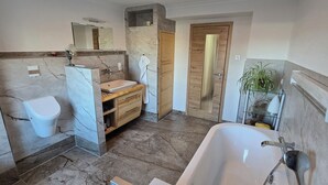 Een moderne badkamer met een marmeren wastafelmeubel, een vrijstaand bad en een houten deur.