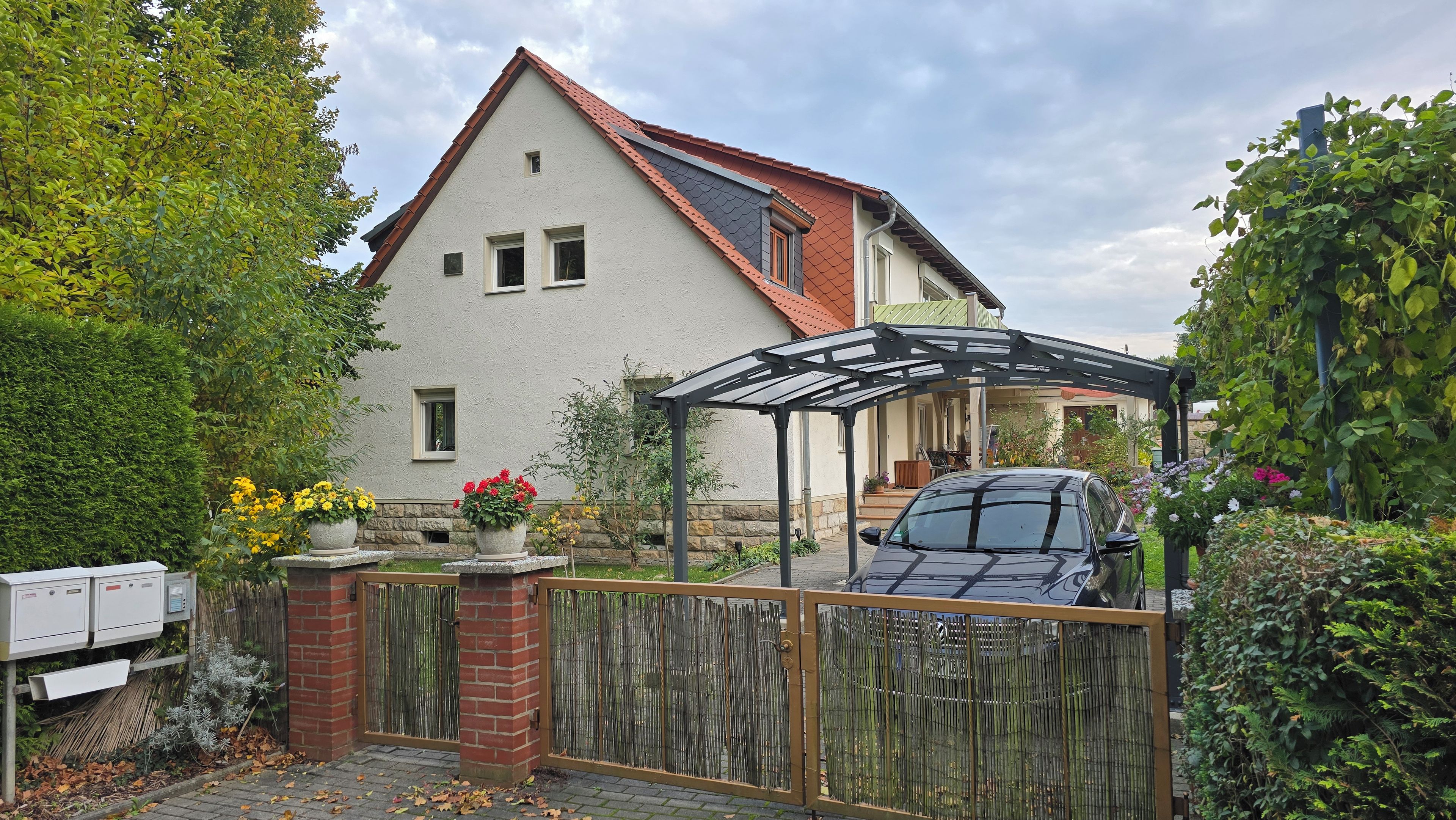 Ein Haus mit überdachter Veranda, ein Auto davor und ein Holzzaun.