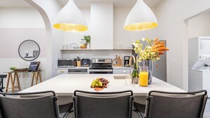Une cuisine moderne dotée d’un îlot central, de meubles blancs et d’un éclairage suspendu.