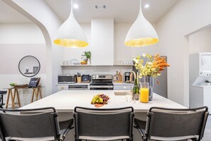 Una cocina moderna con una isla central, iluminación colgante y un comedor con sillas.