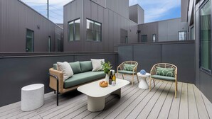 Un espace de détente extérieur moderne, comprenant un canapé, deux fauteuils en osier, une table ronde et un petit tabouret.