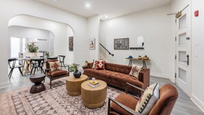 Un salon spacieux avec un canapé marron, deux petites tables rondes et un tapis à motifs.