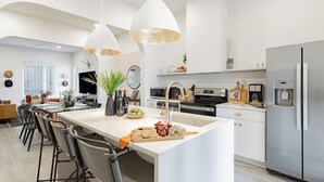 Une cuisine moderne dotée d’un îlot central, d’appareils électroménagers en acier inoxydable, de luminaires suspendus et d’un coin repas avec des tabourets de bar.