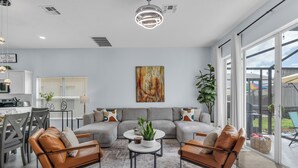 A modern living room with a sectional sofa, leather armchairs, a coffee table, and a dining area with a chandelier. - Spacious 6-bedroom house with Private Pool/Spa, Game Room, & Resort Perks (Clermont)