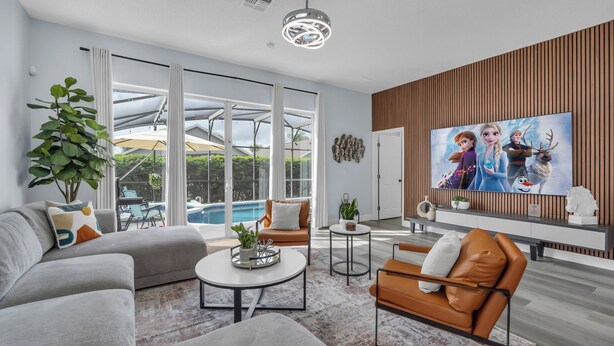 A modern living room with a large TV, comfortable seating, and a view of the outdoors. - Spacious 6-bedroom house with Private Pool/Spa, Game Room, & Resort Perks (Clermont)