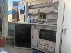 Una kitchenette compacta con microondas, un lavamanos pequeño y armarios para guardar cosas.