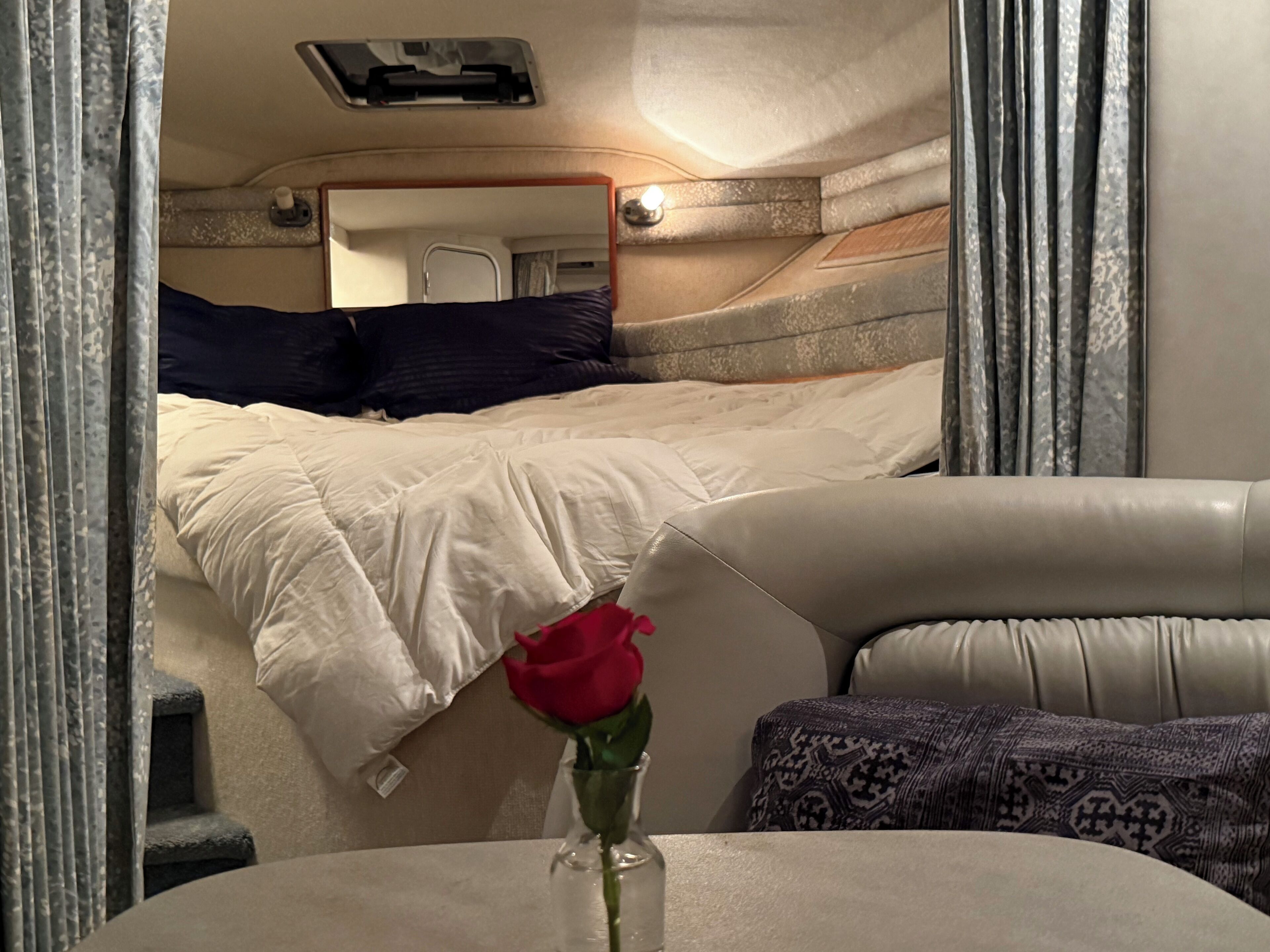 Un intérieur chaleureux avec un lit, une petite table sur laquelle est posé un vase contenant une rose rouge, et un canapé en cuir.