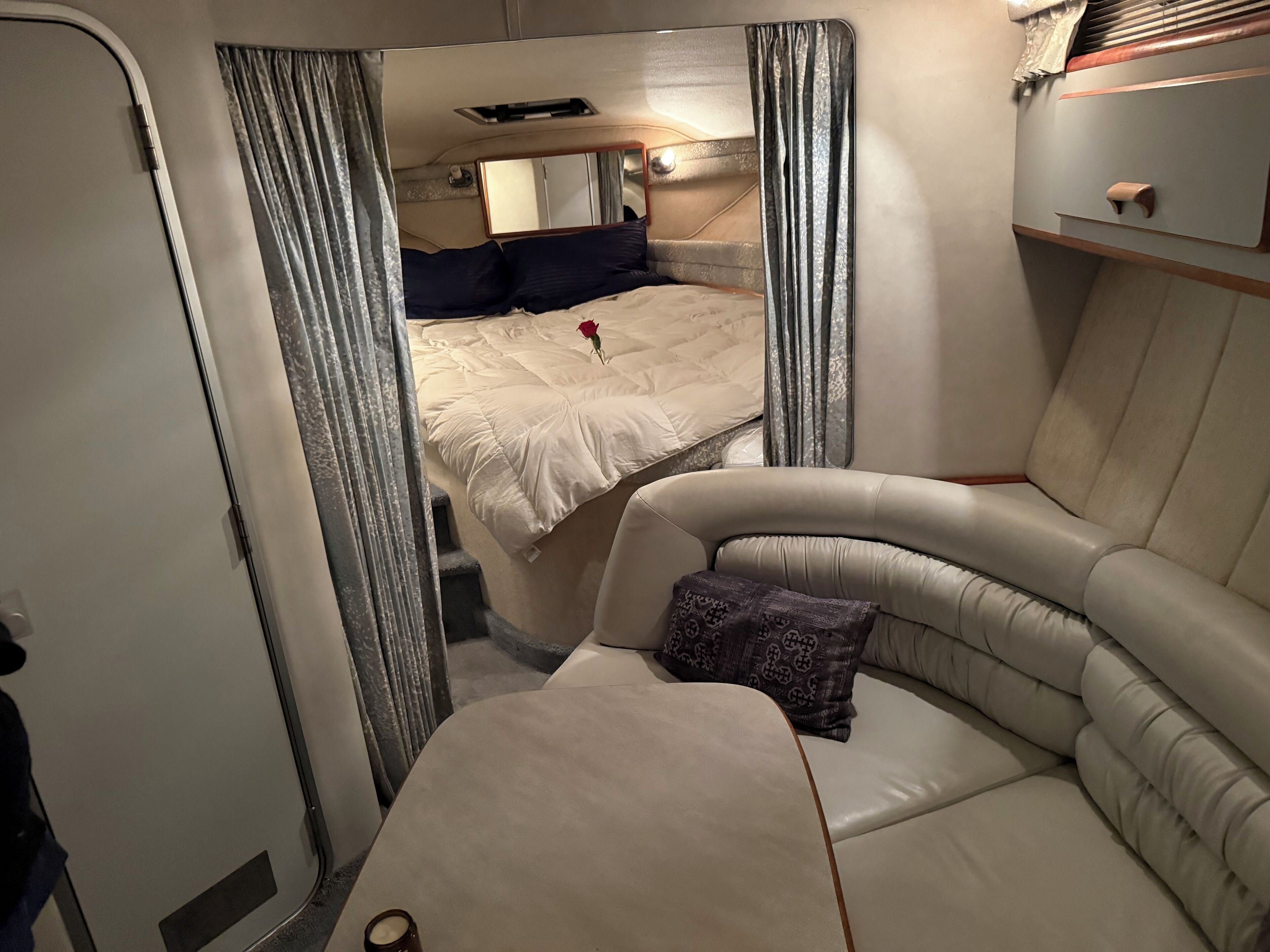 Een compact, goed verlicht interieur met een gebogen bank, een bed met één kussen, en een kleine tafel.