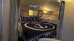 Ein gemütliches Interieur mit einem Bett, das ein nautisches Ankerdesign zeigt, einem kleinen Fenster und einem Spiegel darüber.